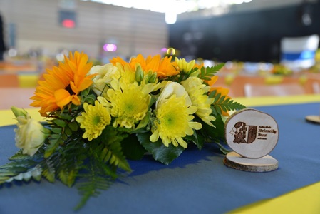 Ein Tisch mit einer bunten Blumenarrangement aus Sonnenblumen, gelben und weißen Blumen sowie einem Holzschild mit der Aufschrift 'Heimelig Baar'.