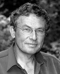 Ein Mann mit Brille und lockigem Haar, der in die Kamera schaut.