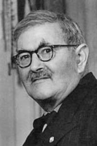 Ein älterer Mann mit Brille und Schnurrbart, der in die Kamera schaut.