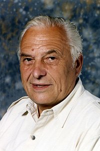 Ein älterer Mann mit grauen Haaren und einem freundlichen Gesichtsausdruck, der in die Kamera schaut.