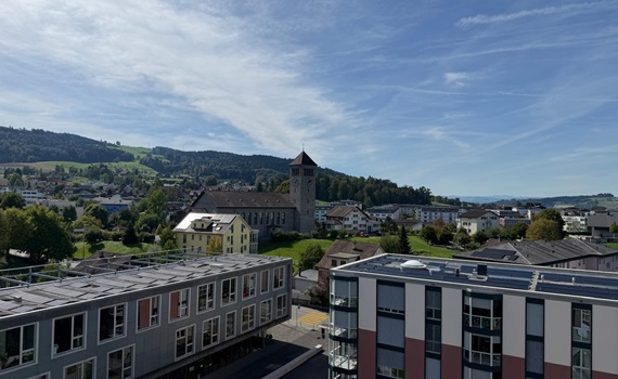 Blick auf eine Stadtlandschaft mit einem historischen Gebäude und modernen Wohnhäusern im Vordergrund, umgeben von Hügeln.