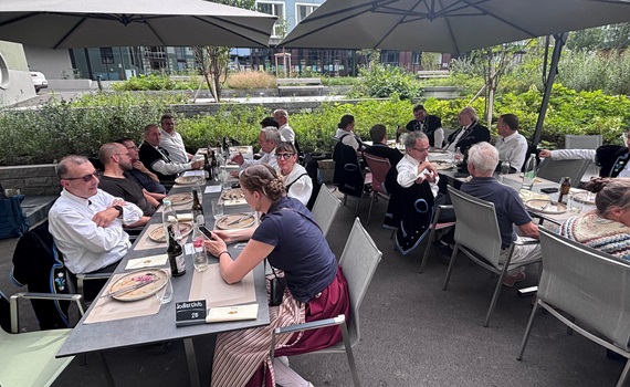 Eine Gruppe von Personen sitzt an einem Tisch im Freien und genießt eine Mahlzeit unter Sonnenschirmen.